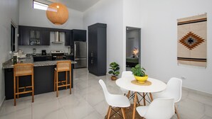 Une cuisine moderne avec des meubles de couleur sombre, un îlot central doté de tabourets, et un coin repas avec une table ronde et des chaises.