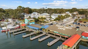 A coastal marina with docked boats, a Fishy Fishy Cafe, and residential buildings in the background.