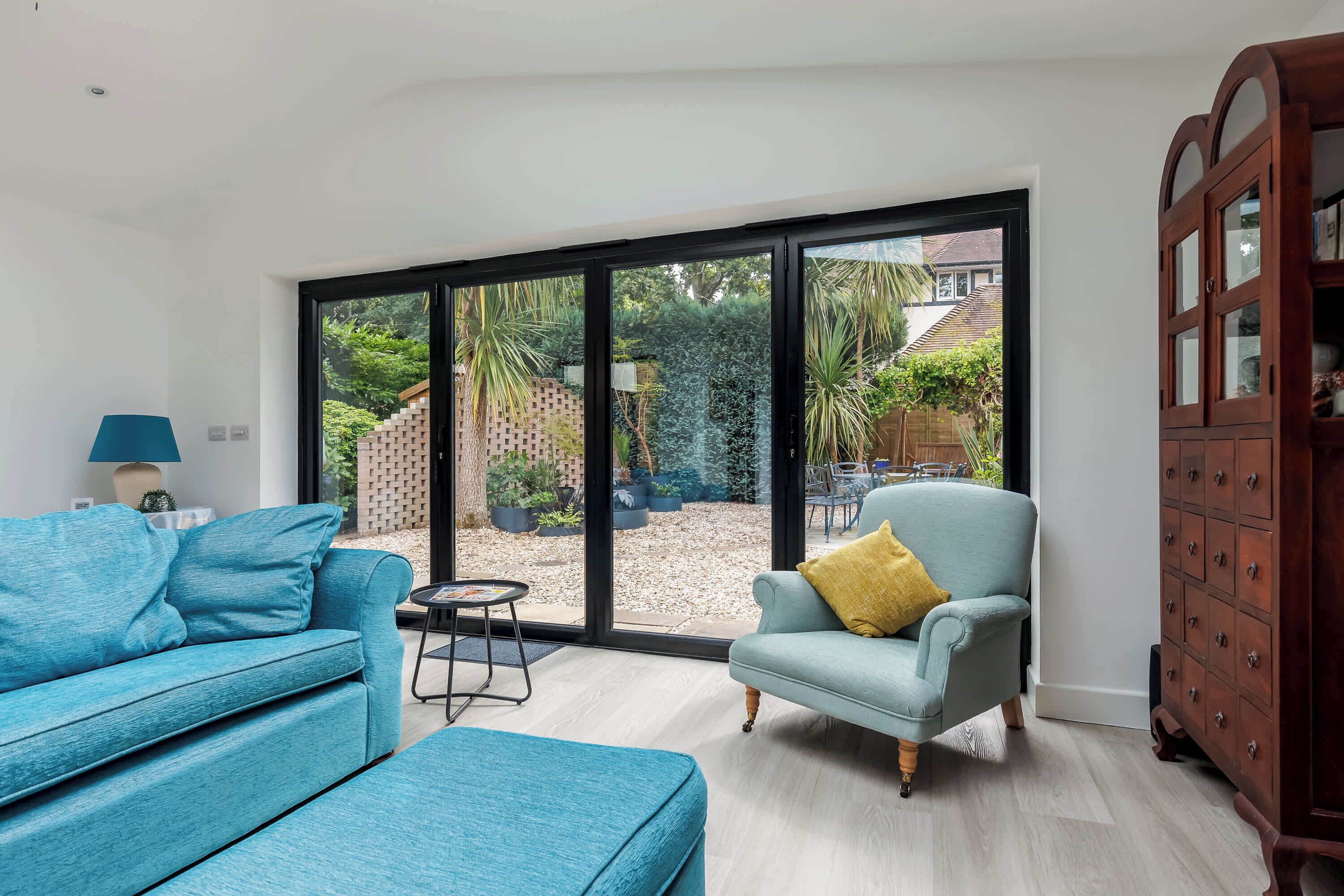 Un salon moderne avec un canapé bleu, un pouf assorti et un fauteuil bleu clair agrémenté d’un coussin jaune. On peut apercevoir un meuble en bois sur la droite.