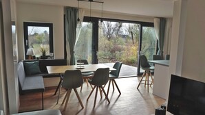 A modern living room with a dining area, large windows, and a flat-screen TV.