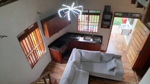 A spacious living area with a white sofa, wooden flooring, and a kitchen with a sink and cabinets. - White Cat Farm Hut Inn (Mashonga)