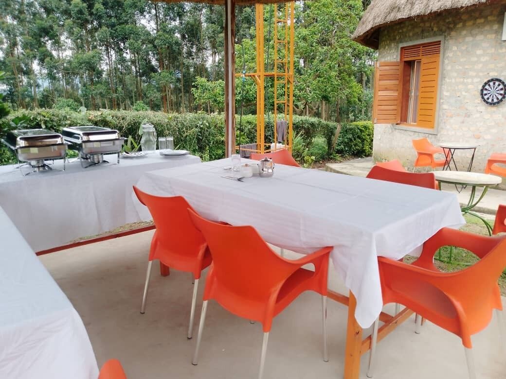 A dining area with a table set for four, surrounded by orange chairs, and a buffet station in the background.