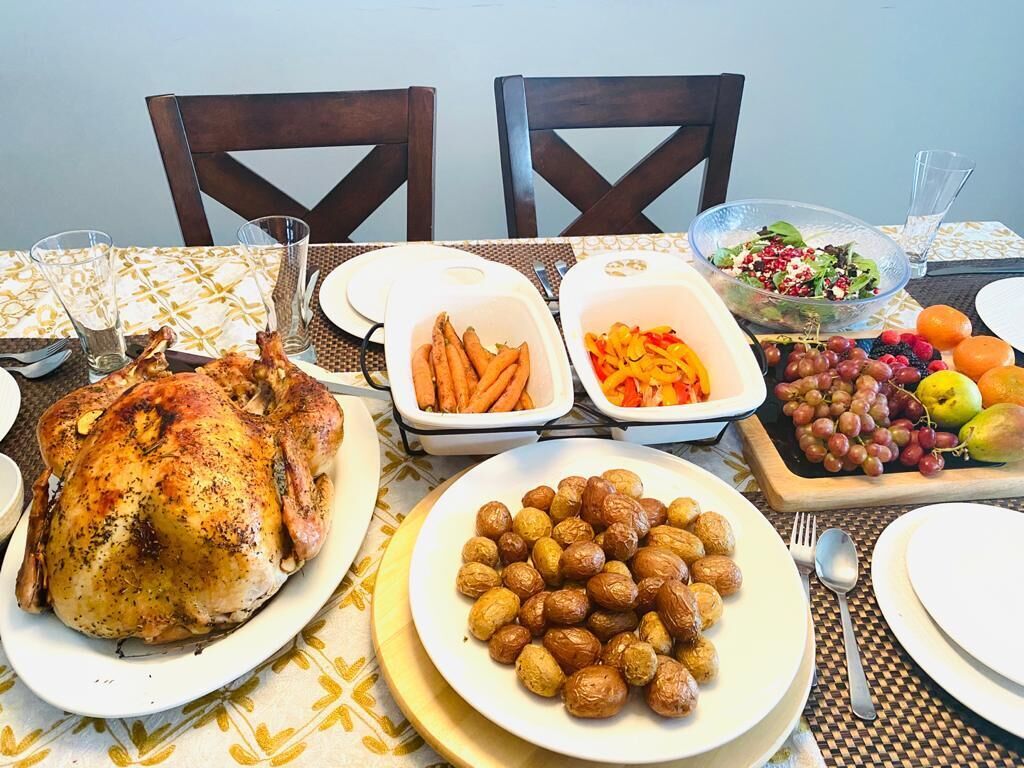 A dining table set with a roasted chicken, roasted potatoes, a salad, and various fruits and vegetables.