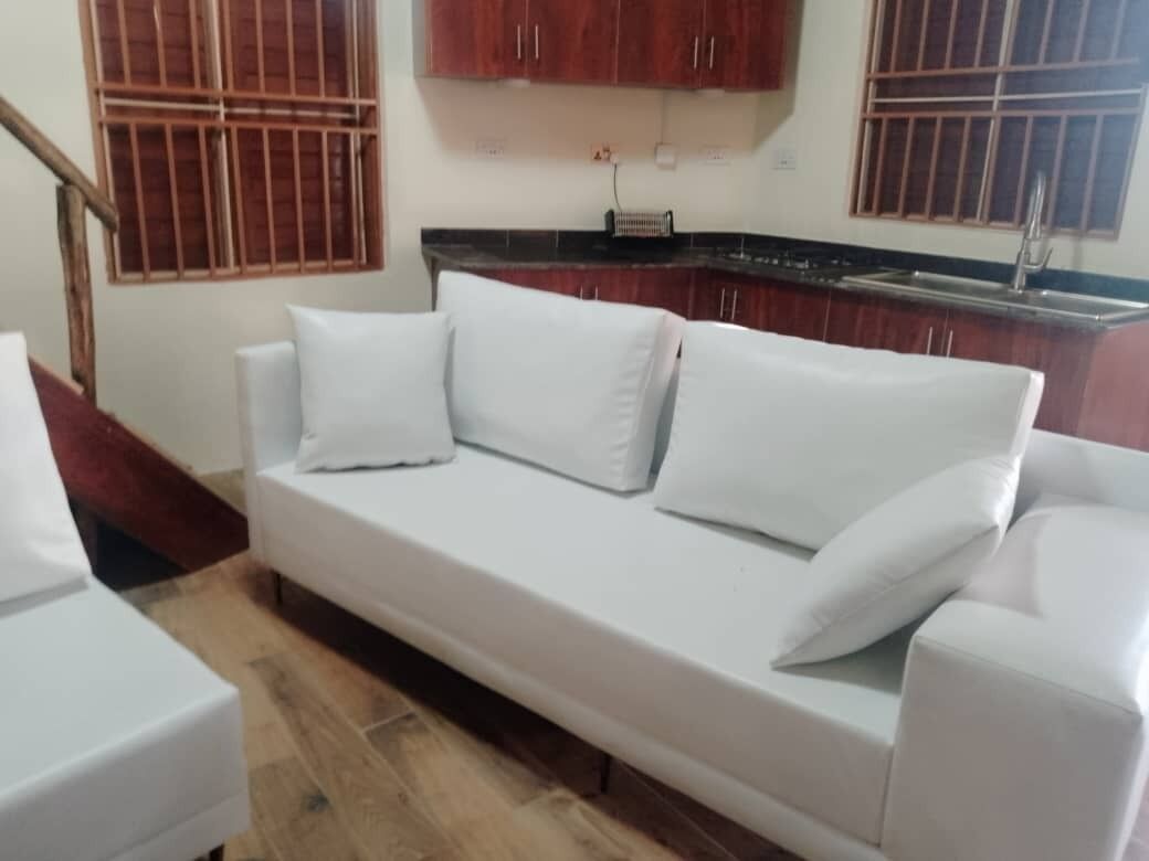 A white sofa in a room with wooden flooring and a kitchen area in the background.