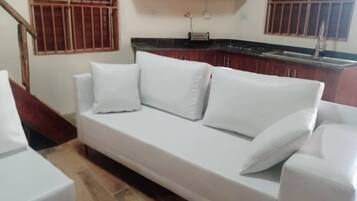 A white sofa in a room with wooden flooring and a kitchen area in the background.