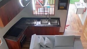A modern living room with a large L-shaped sectional sofa, a wooden dining table, and a unique ceiling light fixture. - White Cat Farm Hut Inn (Mashonga)
