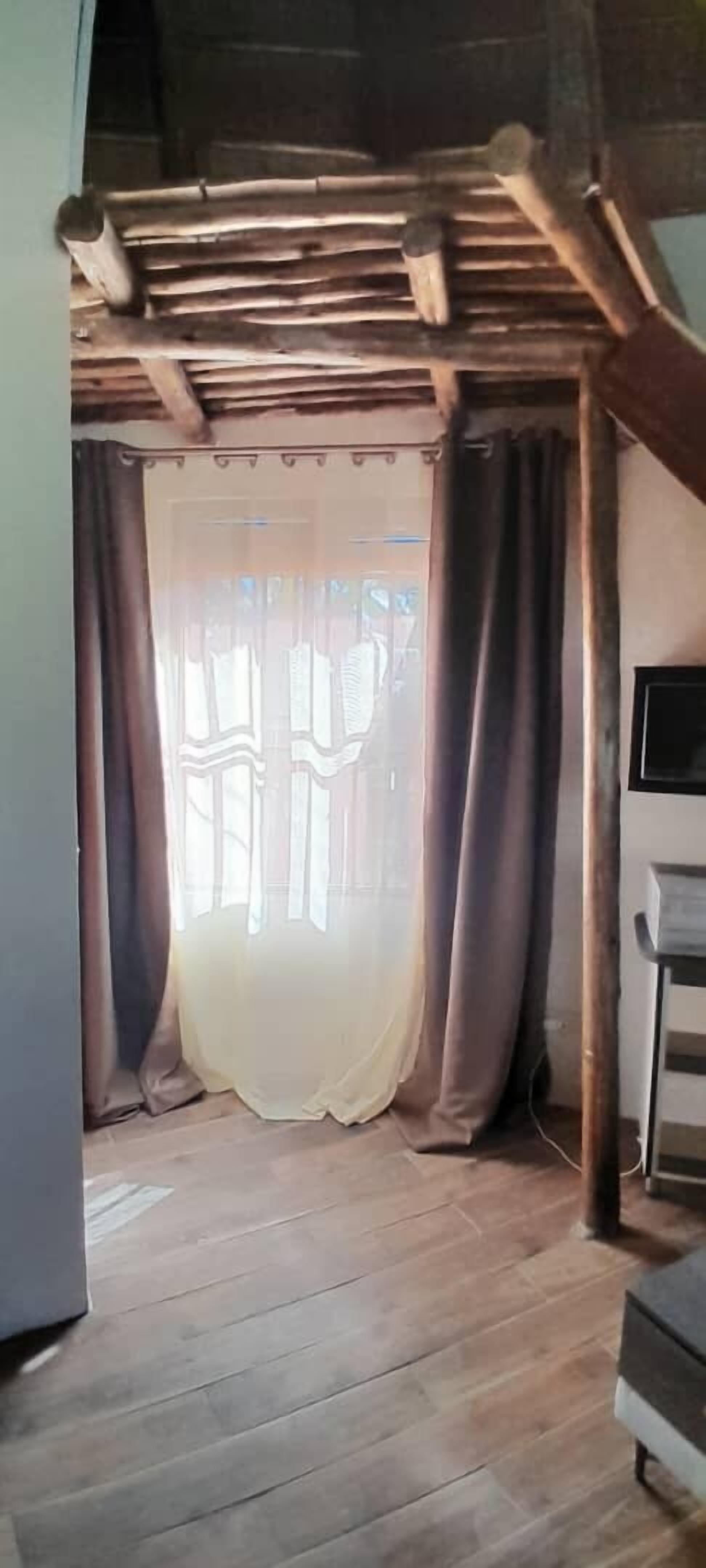 A room with a wooden ceiling, a window with sheer curtains, and a wooden floor.