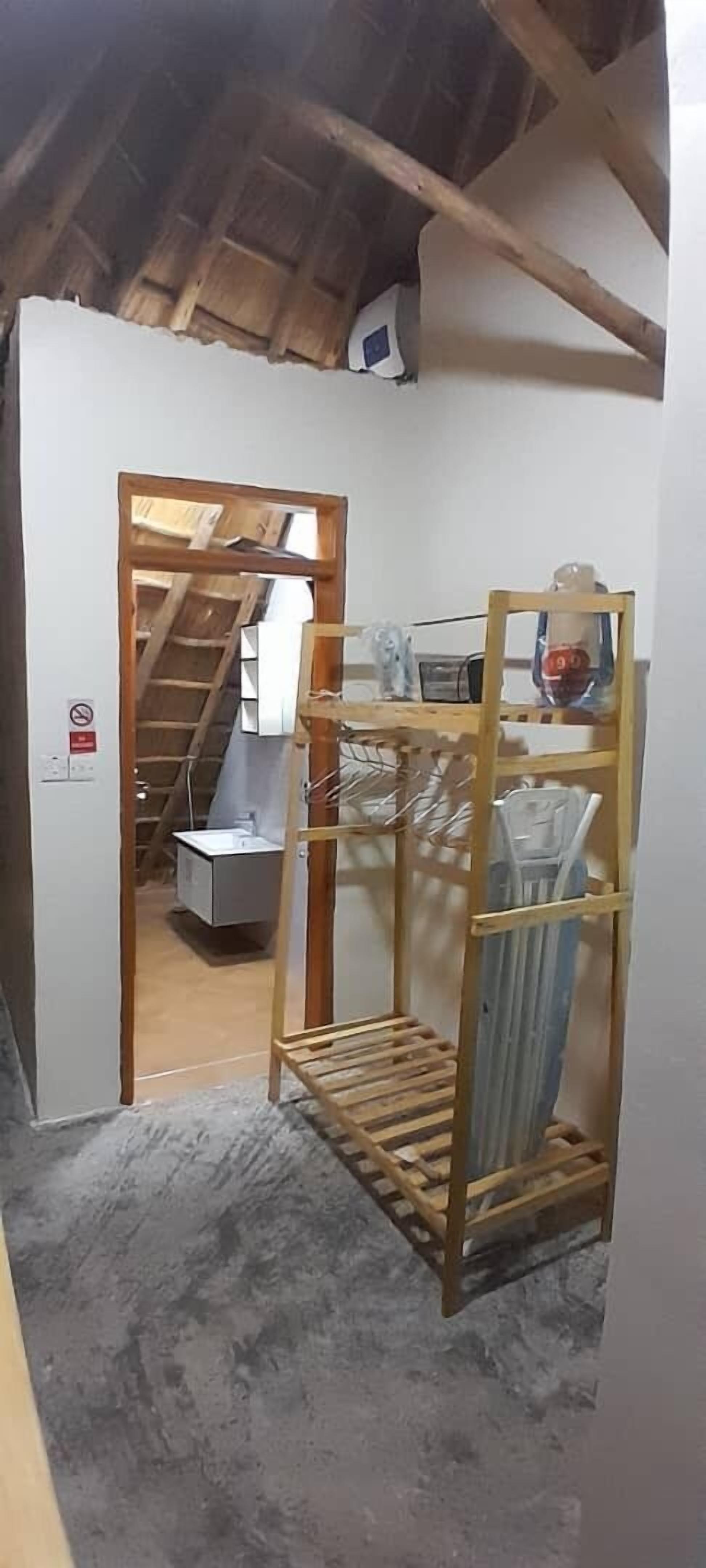 A narrow hallway with a wooden ladder leading to a lofted area. A metal rack with plastic containers is visible in the foreground.