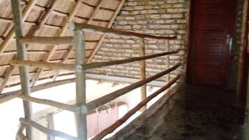 Una habitación con techo de paja, pared de ladrillo y puerta de madera.