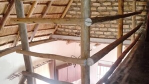 A room with a thatched roof, wooden beams, and a brick wall. There is a window with a view outside. - White Cat Farm Hut Inn (Mashonga)