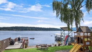A lakeside deck with picnic tables, a children's play area, and a boat dock.