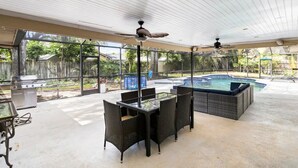 Patio esterno con tavolo e sedie in vetro, una griglia e una vasca idromassaggio.