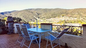 Eine Außenpatio mit Tisch und Stühlen, einem Steingrill und Blick auf eine Hügelstadt.