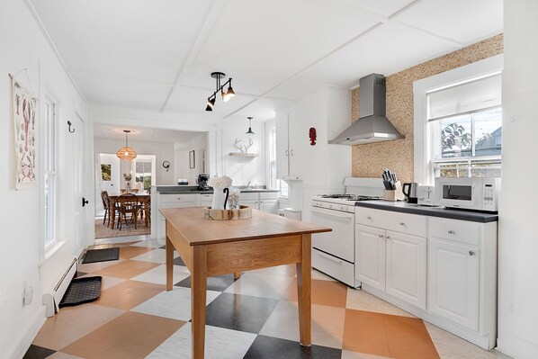 A modern kitchen with white cabinetry, a wooden dining table, and a checkered floor. - Historic Summer's Landing! (Kennebunk)