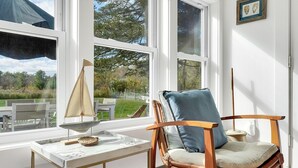 A room with a wooden chair, a small table, and a view of the outdoors through large windows.