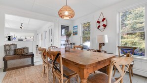 A dining area with a wooden table and chairs, a woven rug, and a hanging light fixture.