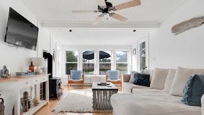 A spacious living room with a white sofa, a television mounted on the wall, and a ceiling fan.