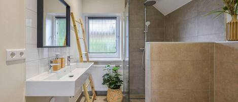 A modern bathroom with a white vanity, a glass shower enclosure, and a potted plant.