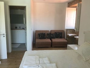 Una camera da letto con un letto, due divani marroni con cuscini decorati, un comodino e un armadietto bianco sopra un lavandino.
