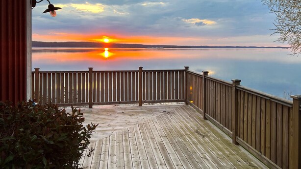 Una terraza de madera con barandilla que da a un lago tranquilo al atardecer.