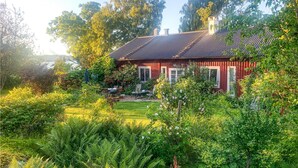 Una casa roja con tejado de tejas, rodeada de abundante vegetación y plantas con flores.