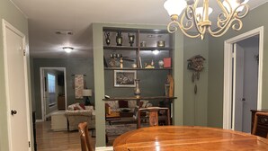 Un coin repas avec une table et des chaises en bois, un lustre et une bibliothèque contenant divers objets.