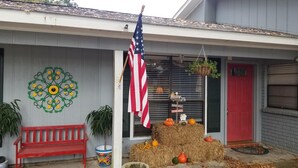 Une maison avec un banc rouge, une fleur décorative en métal, un drapeau américain et une botte de foin ornée de citrouilles et de courges.