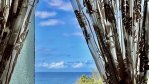 Une vue à travers des rideaux légers, avec une plage tropicale et l’océan en arrière-plan.