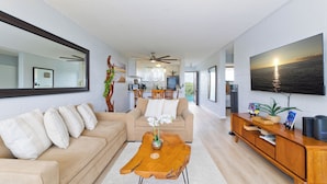 Un salon moderne avec un canapé beige, une table basse en bois et un grand téléviseur à écran plat fixé au mur.