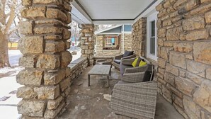 A stone exterior wall, a covered porch with wicker furniture, and a window with a view of a building.
