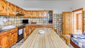 Une cuisine avec des meubles en bois, un pare-feu en carrelage, une table à manger et un téléviseur.