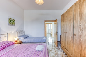 Une chambre à coucher comprenant un lit, une table de chevet, une lampe, une armoire et une porte donnant sur une autre pièce.