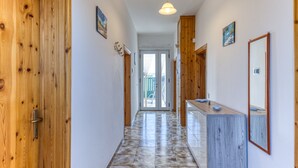 Un couloir avec des portes en bois, un sol carrelé, un comptoir en bois avec un miroir et un luminaire au plafond.