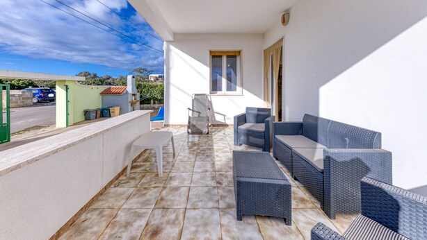 Un espace extérieur abrité, aménagé avec des meubles en osier, une petite table et une fenêtre.