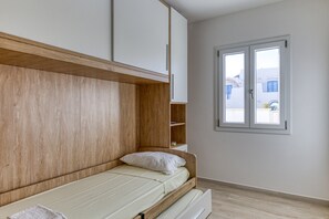 Une chambre à coucher avec une tête de lit en bois, un lit simple, une fenêtre et une vue sur les bâtiments à l’extérieur.