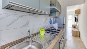 Une cuisine moderne dotée d’un évier en acier inoxydable, d’une cuisinière à gaz et de carreaux de marbre de couleur claire.