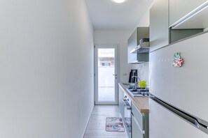 Une petite cuisine étroite avec une porte donnant sur l’extérieur, une cuisinière et un réfrigérateur.
