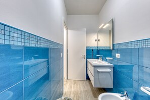 Ein Badezimmer mit blauen Fliesen, einem weißen Waschbecken, einem Spiegel und einer weißen Toilette.