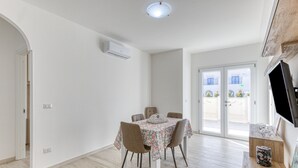 Un coin repas avec une table dressée pour quatre personnes, un luminaire au plafond et une vue à travers des portes vitrées.