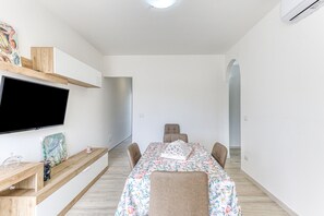 Un espace repas moderne avec un téléviseur à écran plat, des étagères en bois et une nappe à motifs floraux.