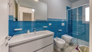 Une salle de bain moderne avec un lavabo blanc, un bidet, des toilettes et une douche à parois de verre.