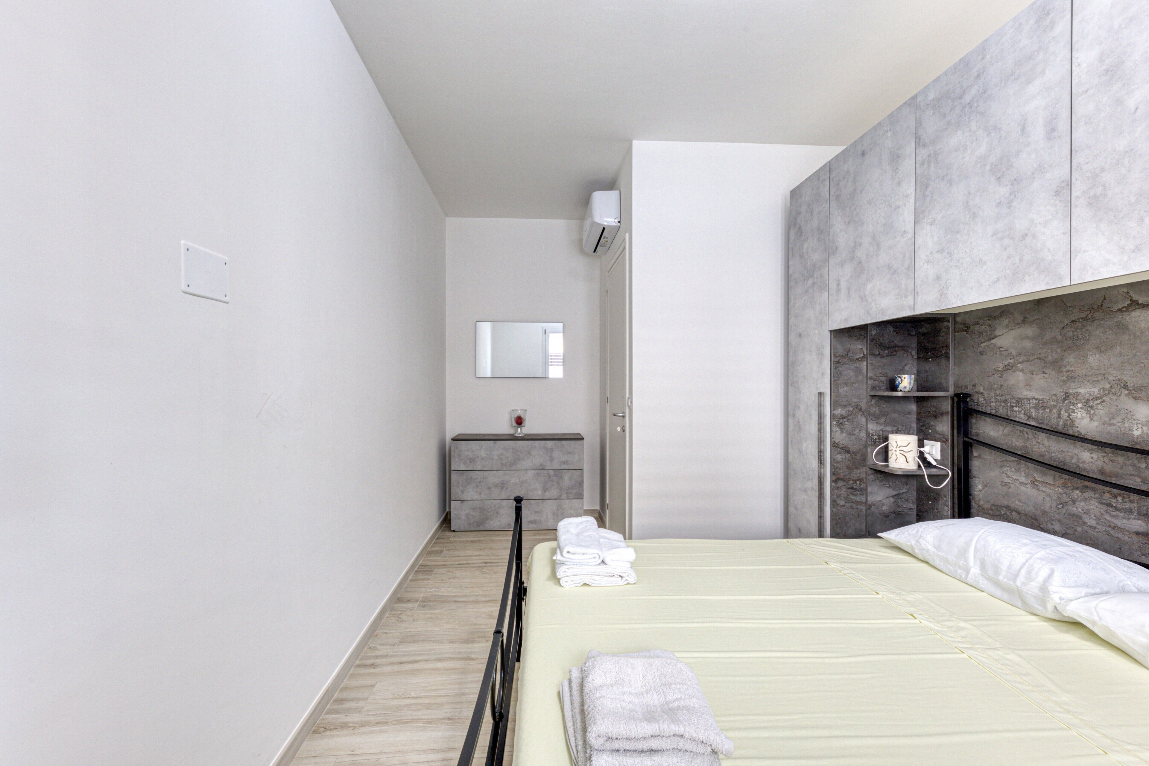 A modern bedroom with a bed, bedside tables, a mirror, and a wardrobe.