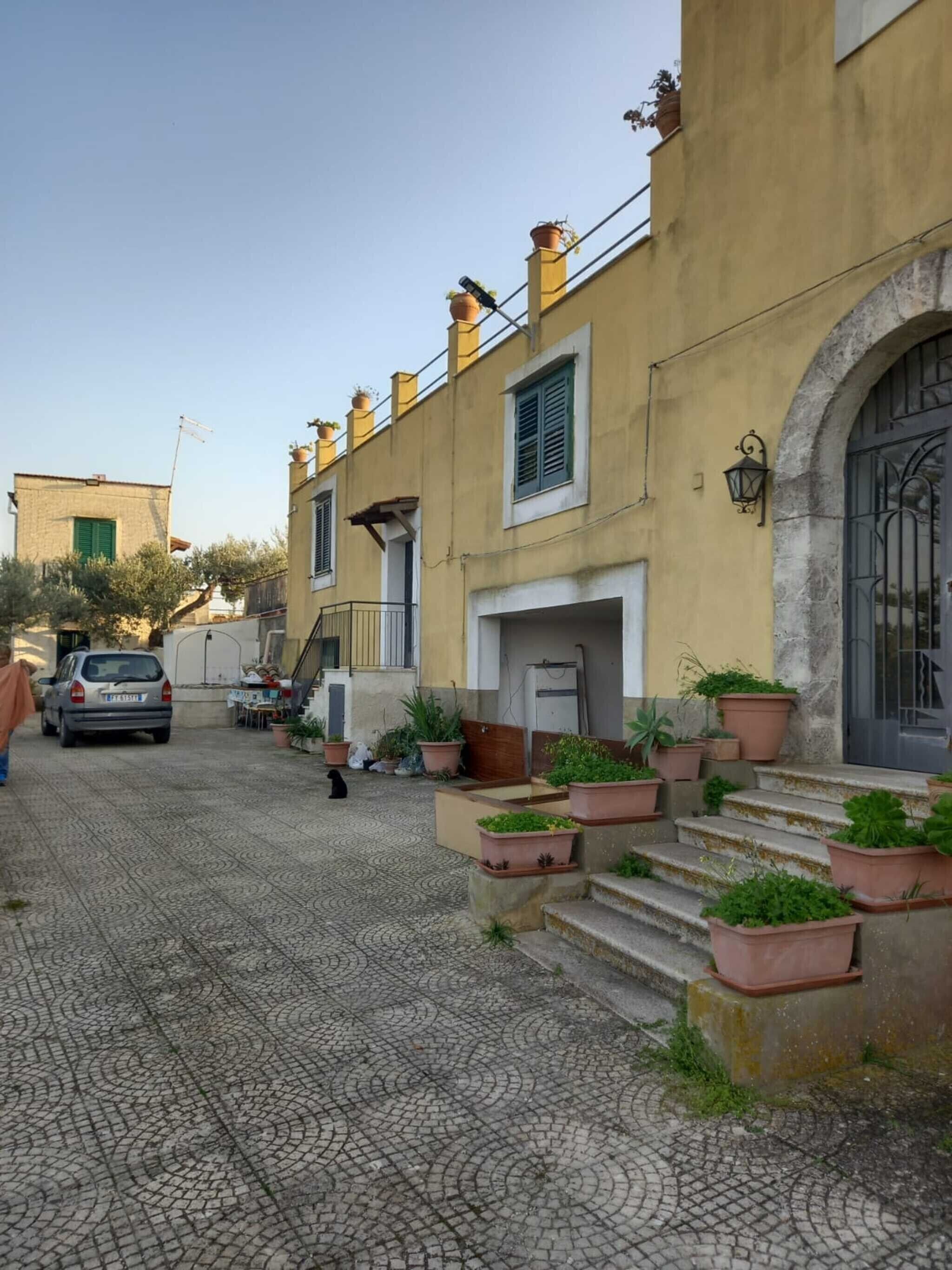 A building with a tiled courtyard, a car parked in front, and a person walking.