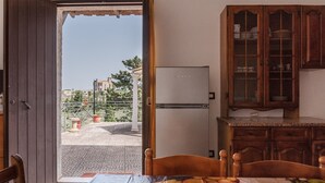An open door leading to an outdoor area with a view of buildings and trees, a refrigerator, wooden cabinets, and a table with a fruit-patterned tablecloth. - Pet-Friendly Villa 'Rosa' with Sea View & Terraces (Licata)