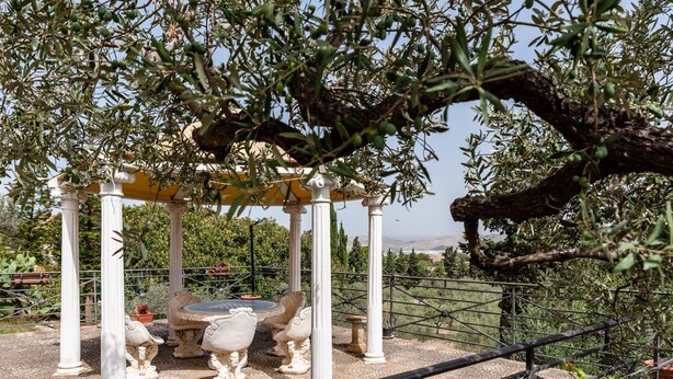 A gazebo with white columns and ornate stone carvings, surrounded by olive trees and a fenced garden area. - Pet-Friendly Villa 'Rosa' with Sea View & Terraces (Licata)