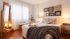Une chambre d’hôtel comprenant un lit, des tables de chevet, un miroir, une fenêtre avec des rideaux et des œuvres d’art accrochées au mur.