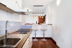 A modern kitchen with a stainless steel sink, wooden countertop, and two white bar stools.