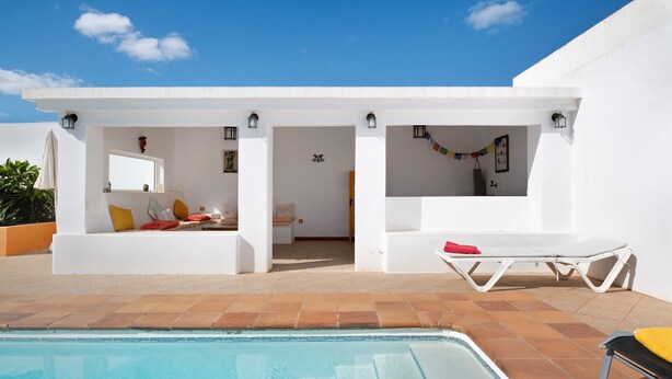A modern outdoor pool area with a clear blue sky, white walls, and a tiled floor.