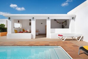 A modern outdoor pool area with a clear blue sky, white walls, and a tiled floor.