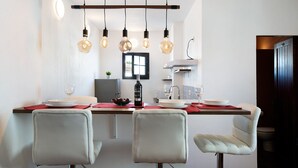 A dining area with a long table, four chairs, hanging light bulbs, and a window.